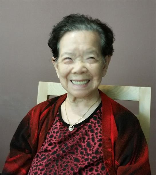 An elderly woman with a joyful smile sits comfortably, radiating warmth and happiness indoors.