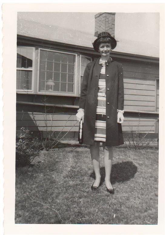 A woman in a dress and hat standing in front of a house