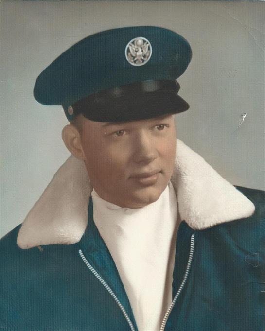 A young man in military attire stands confidently with a warm smile and friendly vibe.