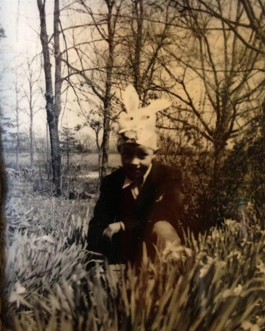 A boy enjoys a moment outdoors, dressed in a bunny hat and playing in blossoming flowers.