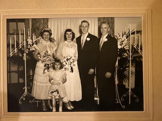A joyful family stands together, dressed elegantly for a wedding celebration, surrounded by flowers.