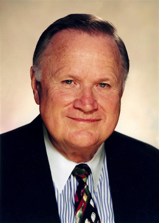 Senior man presents a friendly demeanor while dressed in formal attire against a neutral background.