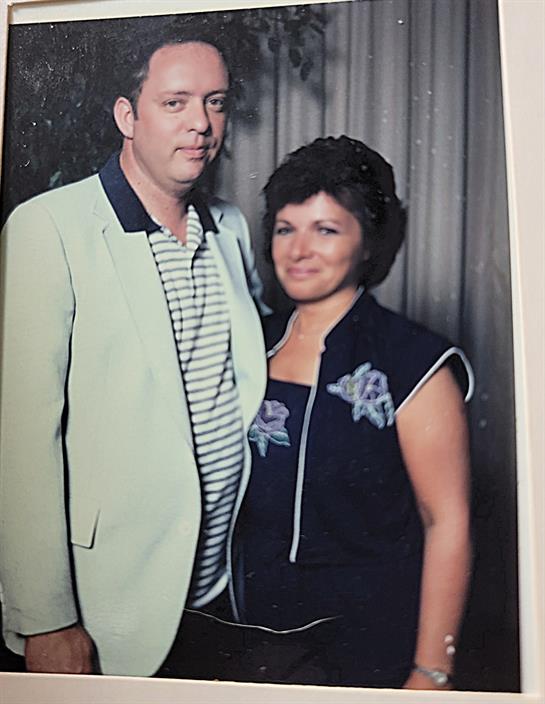 A couple stands together, dressed in fashionable attire, smiling warmly during a joyful occasion.