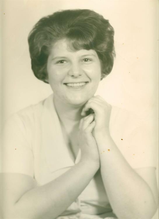 A young woman with a bright smile is resting her chin on her hands, exuding joy.