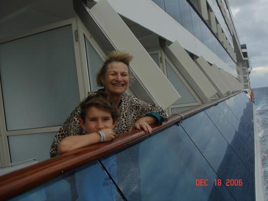 A happy woman and a young boy lean over the railing of a cruise ship, enjoying the ocean breeze.