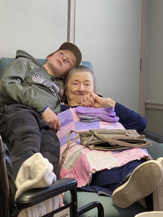 A young boy sits beside an elderly woman, both enjoying a moment of connection and comfort.