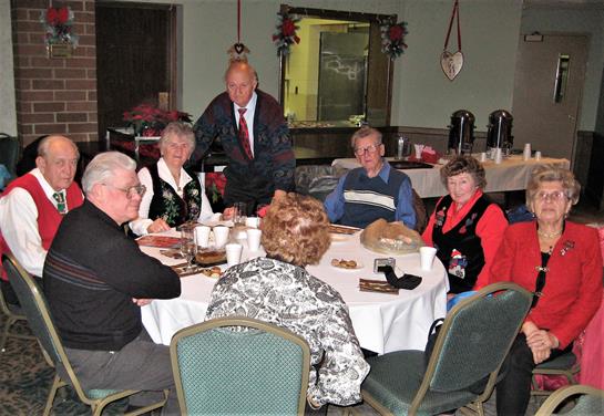 A group of seniors socializes and shares stories at a festive holiday gathering in a cozy venue.