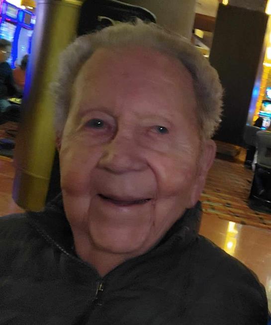 An elderly man smiles cheerfully, surrounded by bright lights and gaming machines.