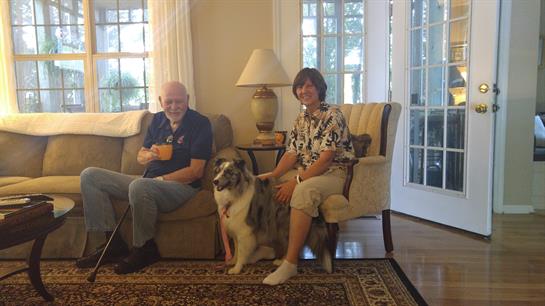 Two friends relax on a couch with a dog, enjoying each other's company in a warm living space.