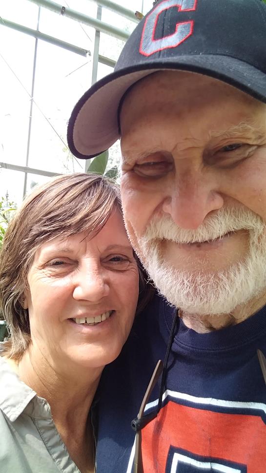 A cheerful couple poses closely in a vibrant greenhouse filled with plants.