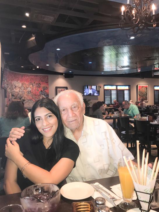 A woman joyfully hugs an elderly man while they share a meal in a busy restaurant.