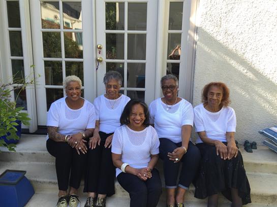 Five women sit together on steps, sharing laughter and stories in a warm, inviting atmosphere.