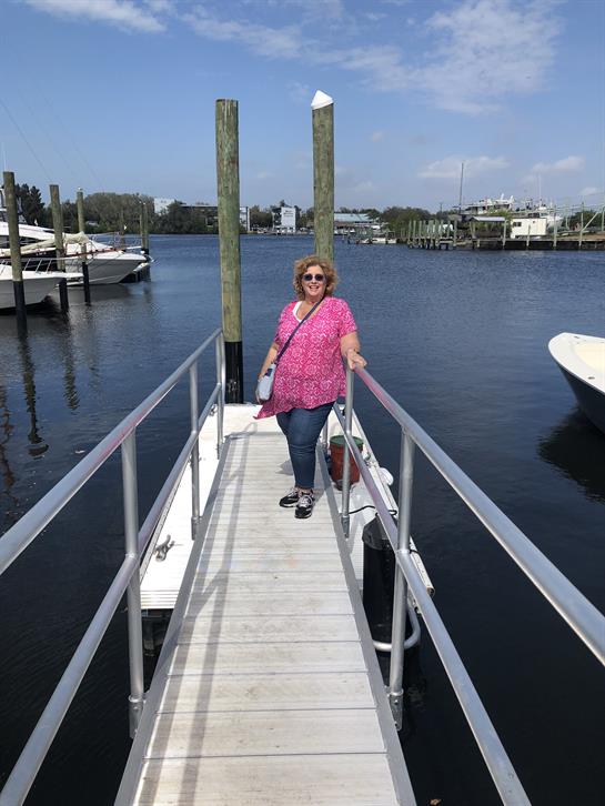A woman enjoys a sunny day on a dock, surrounded by boats and water at the marina.