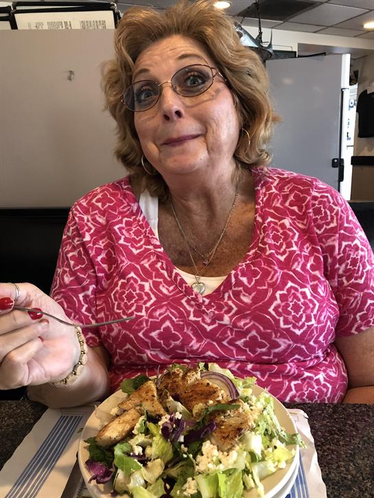 A cheerful woman savors a delicious salad at a local restaurant during lunch.