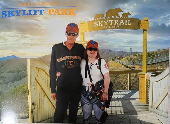 A couple stands happily at SkyLift Park, overlooking a stunning mountain vista at sunset.