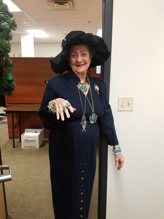 A woman in a stylish dark dress and hat is cheerfully welcoming visitors in an office.