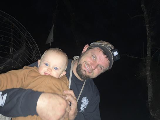 A father joyfully cradles his baby in the darkness, highlighting their bond in a natural setting.