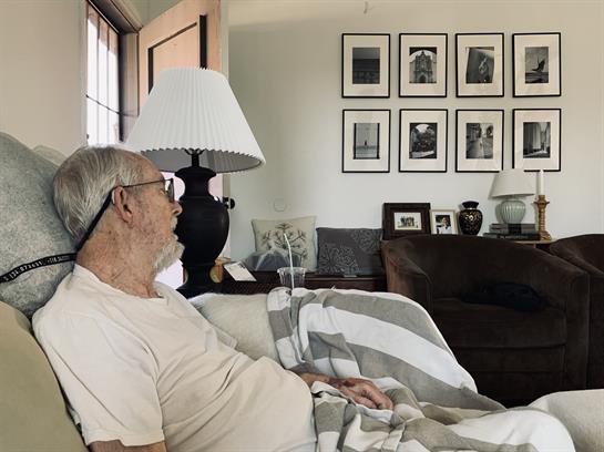 An elderly man relaxes on a sofa, enjoying a peaceful moment in a cozy, memory-filled living room.