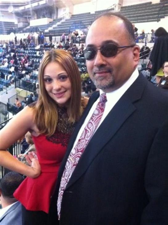 A man and a young woman stand together, smiling, in a large indoor venue filled with spectators.