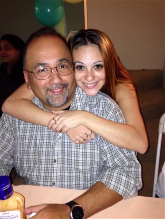 A daughter embraces her father, both smiling happily at a festive family event.