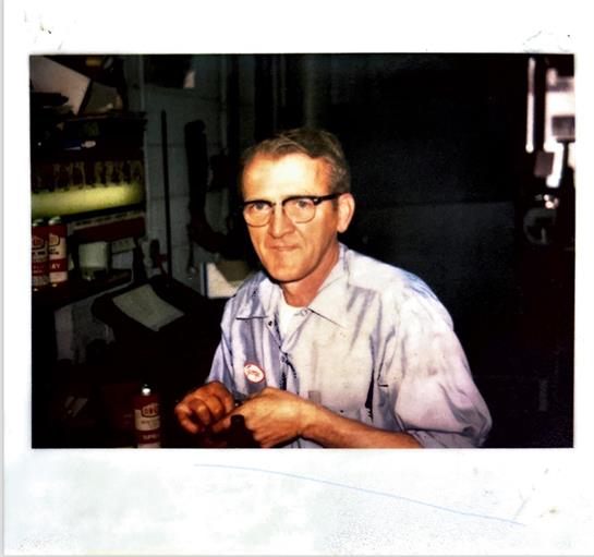An older man meticulously completes a hands-on task in a workshop filled with tools.