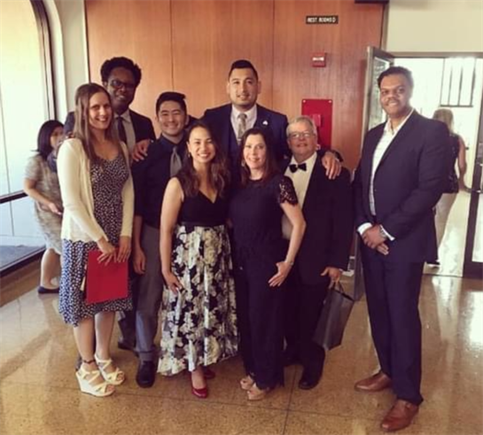 A diverse group poses together in formal attire, celebrating a special occasion in a bright venue.