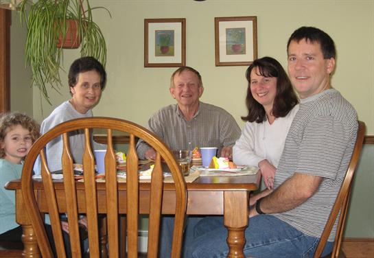 Group of five adults and a child enjoying a meal together at a dining table in a warm setting.