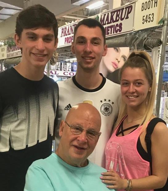 Four individuals stand together, smiling in a busy marketplace filled with various stalls.