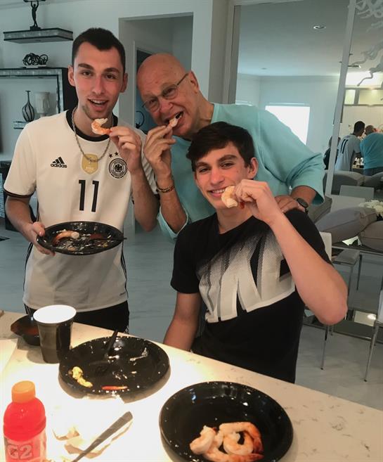Three people share laughter and pastries at a table filled with food in a cozy setting.