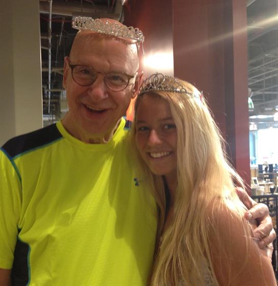 Two happy individuals pose together, both wearing tiaras in a cheerful café setting.