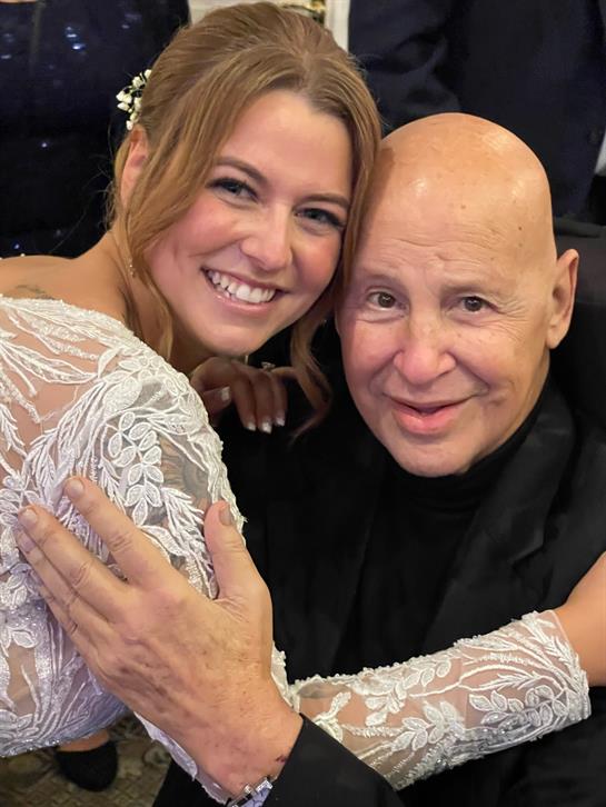 A bride in a beautiful lace dress shares a warm hug with a guest at a wedding celebration.