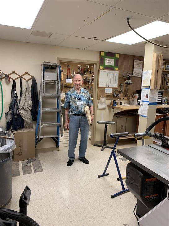 Individual in a woodworking shop displays a completed wooden piece, surrounded by tools.