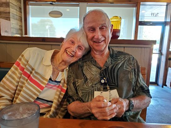 An elderly couple enjoys their time together, smiling and embracing in a warm restaurant setting.