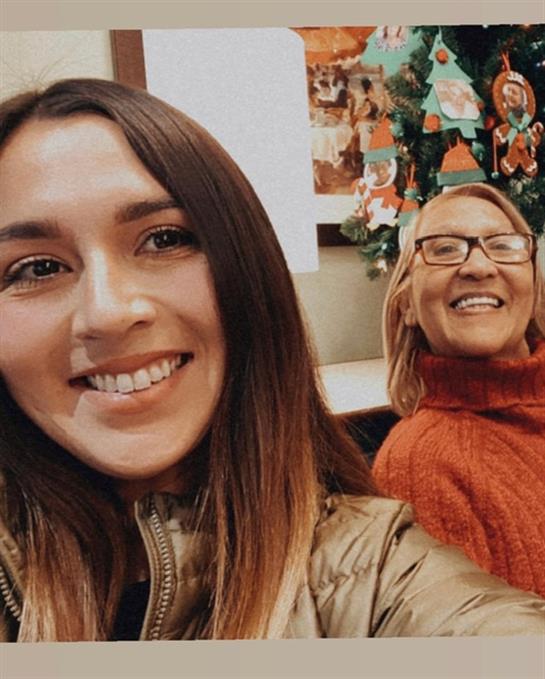 Two women pose happily together in a festive atmosphere with holiday decorations around.
