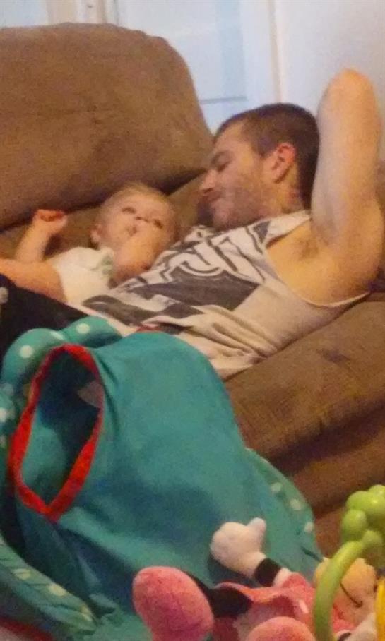 A young father lounges on a couch with his baby, exchanging smiles and playful interactions.