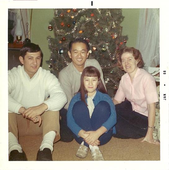 Four family members smile on the floor in front of a decorated Christmas tree.