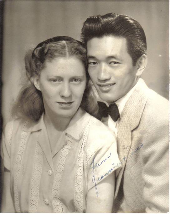 A couple dressed in elegant attire share a close, affectionate moment in a vintage background.