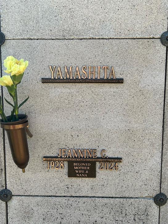 Flowers placed beside an engraved plaque commemorating Jeannine C Yamashita in a mausoleum.