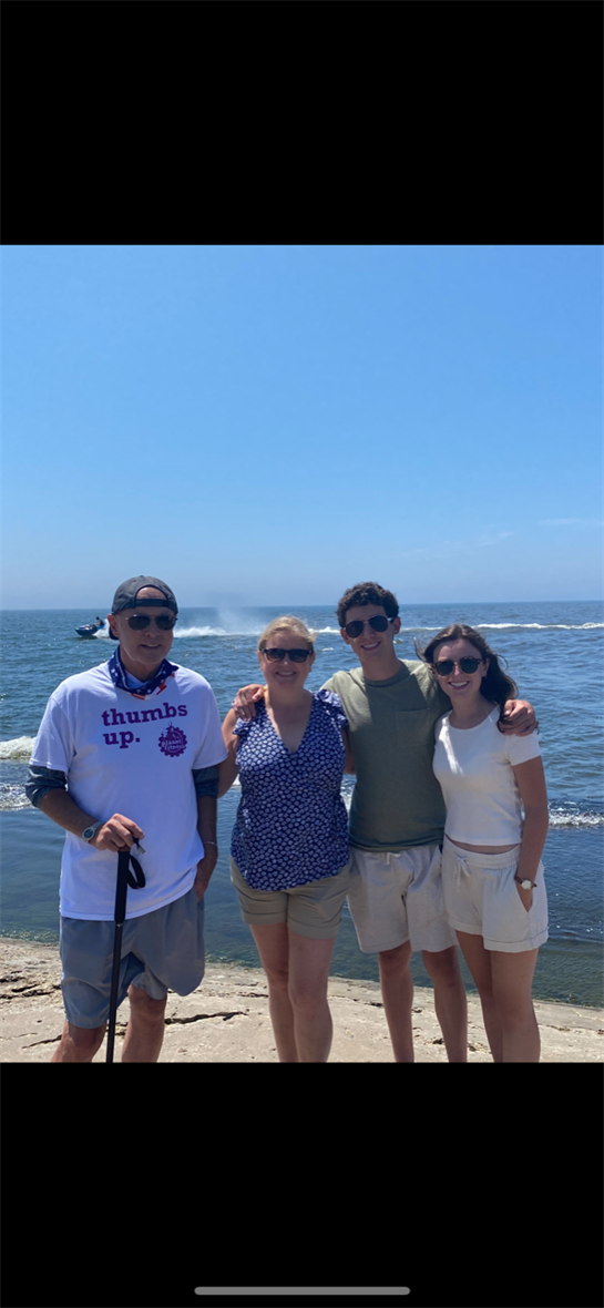 Four family members stand on the beach with a beautiful ocean background, smiling happily.
