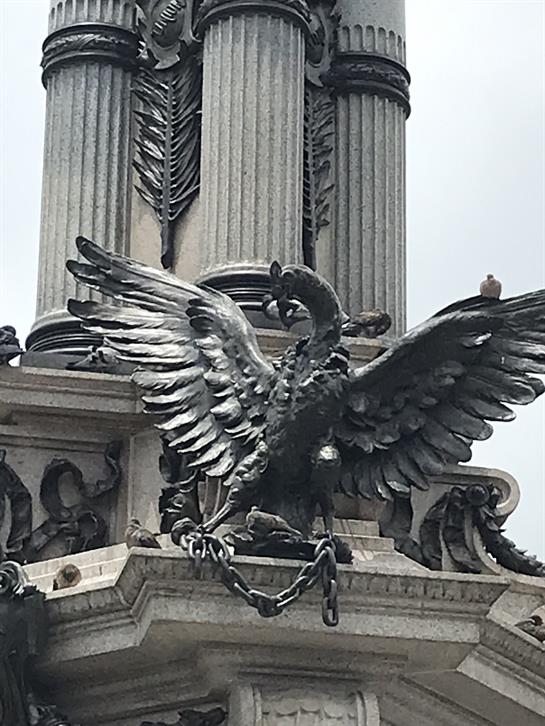 Eagle sculpture with outstretched wings sits above ornate columns in a public square.