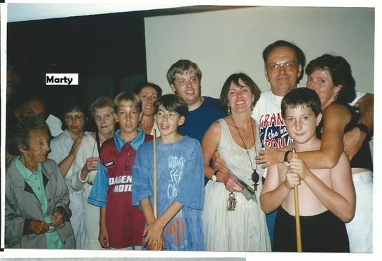 A group of friends and family gathers indoors, smiling and enjoying each other’s company.
