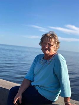 A woman smiles while sitting on a pier, surrounded by serene water and a clear sky.