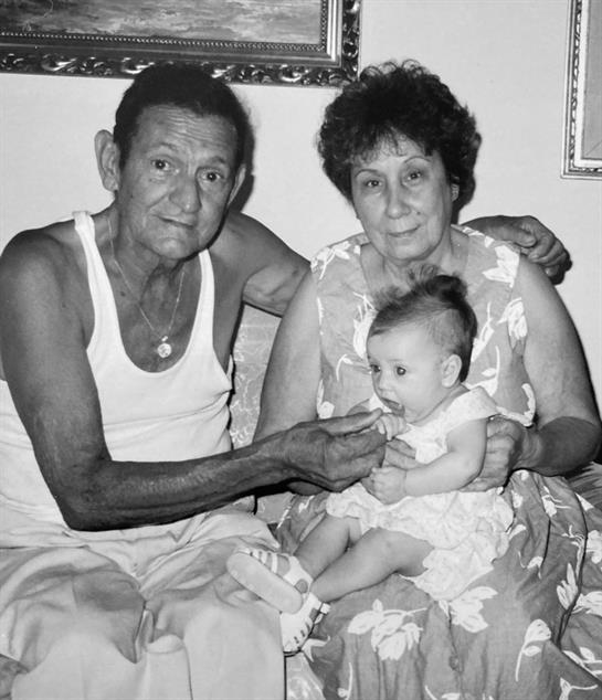 Grandparents interact lovingly with their granddaughter while sitting on a couch at home.