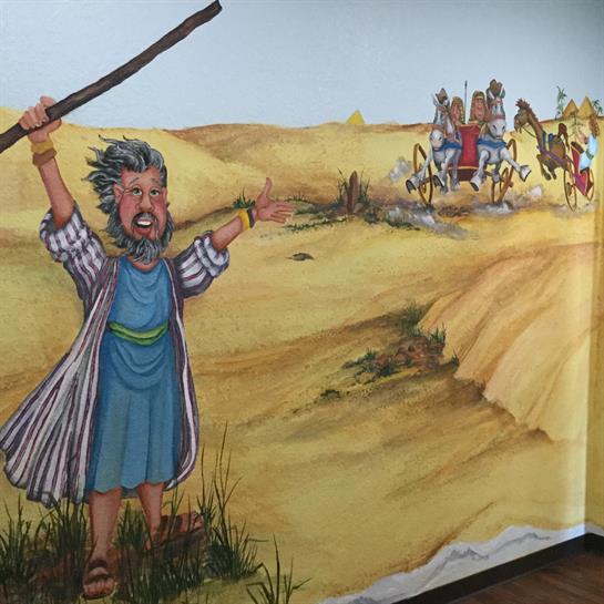 A vibrant mural depicts a biblical figure signaling a chariot in the desert.