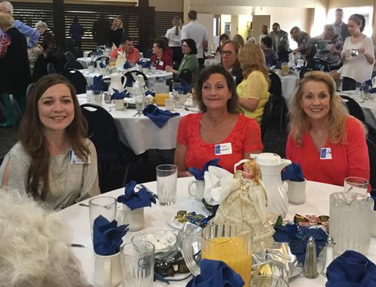 Three women enjoy each other's company at a decorated table, surrounded by fellow attendees.