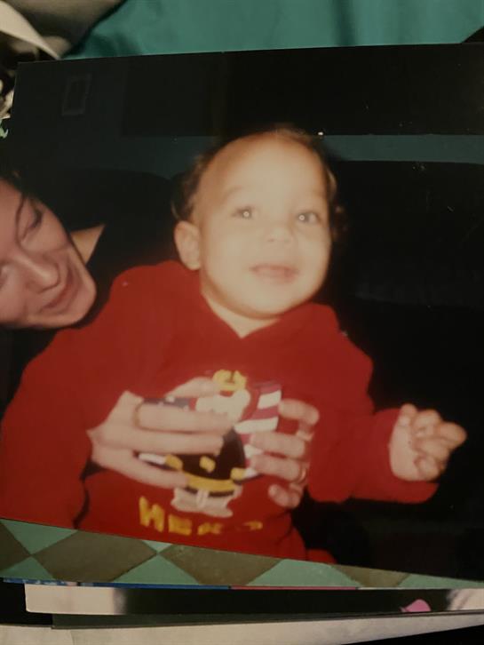 A joyful child in a red hoodie is embraced by an adult, both smiling in a cozy setting.