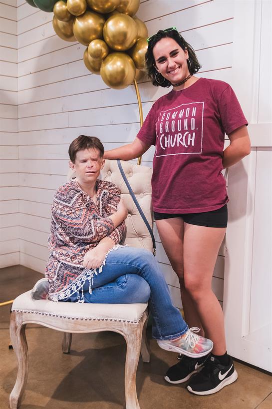 Two women share a moment in a warmly decorated space, surrounded by festive balloons.