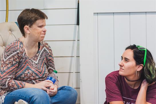 Two women are sitting on the floor, sharing a thoughtful conversation and smiles.