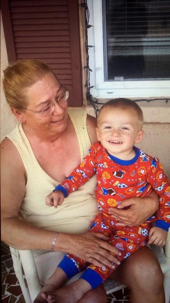 A grandmother smiles lovingly at her grandson, who is wearing colorful pajamas, on a porch.