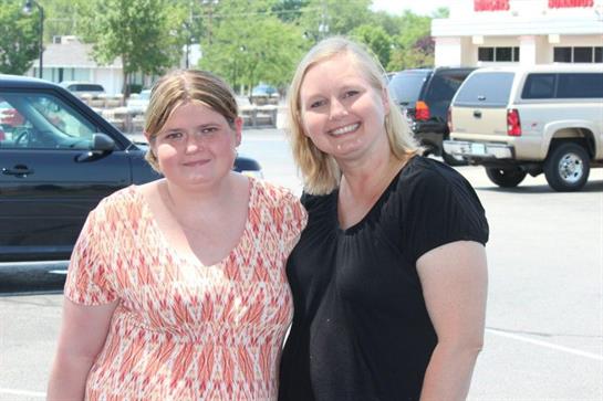 Two women stand happily in a parking lot under clear skies, enjoying their time together.